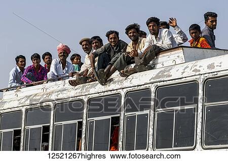 Stock Photograph - A bus full of people and passengers riding on the roof; Jaisalmer, Rajasthan, India. Fotosearch