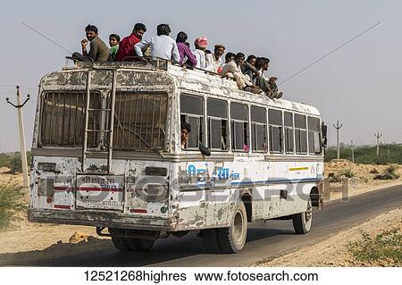 Stock Photograph - A bus full of people and passengers riding on the roof; Jaisalmer, Rajasthan, India. Fotosearch