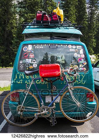 Stock Photograph - A camper van in a parking lot covered with bumper stickers and graffiti, and with a luggage on a rack and bike on the back; Field, Alberta, Canada. Fotosearch
