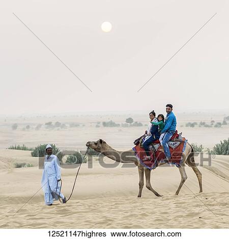 Stock Photograph - A family on a camel safari on the Lakhmana Dunes; Damodara, Rajasthan, India. Fotosearch