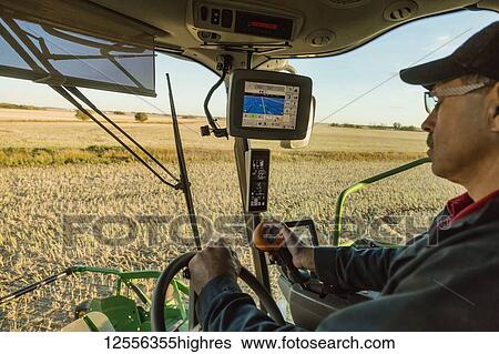 Stock Photograph - A farmer in the cab of his combine harvesting Canola at sunset and using computer automation in his equipment; Legal, Alberta, Canada. Fotosearch