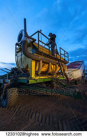 Stock Photograph - A Farmer Works On His Farming Equipment At Dusk; Washington, United States Of America. Fotosearch