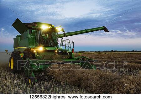 Stock Photograph - A fully loaded combine with its lights on arm out for transer, harvesting canola after sunset; Legal, Alberta, Canada. Fotosearch