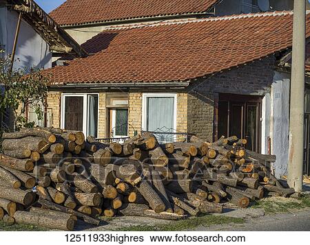 Stock Photograph - A house with a large pile of cut logs in the front yard and heavy equipment on the roof; Kladovo, Bor District, Serbia. Fotosearch