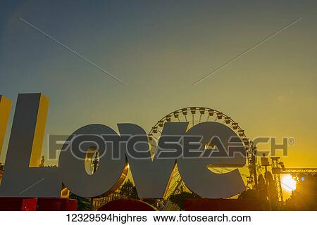 Stock Photograph - A Large Sign Reading Love With A Silhouette Of A Ferris Wheel Against A Golden Sky At Sunset, Place Massena; Nice, Cote D'azur, France. Fotosearch