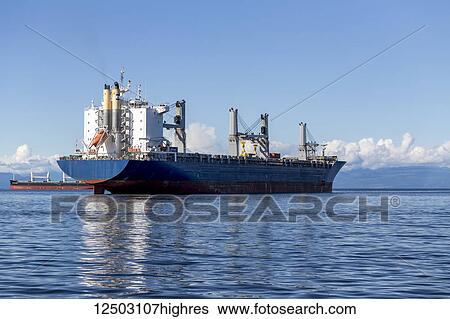Stock Photograph - A large vacant container ship is anchored outside of Vancouver waiting to transport goods from the Port of Vancouver to overseas markets; Vancouver, British Columbia, Canada. Fotosearch