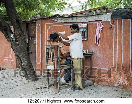 Stock Photograph - A man shaving another man's face with a set up of table and chair along the street; Jaipur, Rajasthan, India. Fotosearch