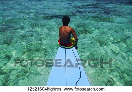 Stock Photograph - A man sits on a blue platform looking out the the clear, turquoise waters; Andaman Islands, India. Fotosearch