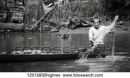 Stock Photograph - A man smoking a cigarette while fishing from his boat on the Mekong River, Mekong Delta; Thoi An, Can Tho, Vietnam. Fotosearch