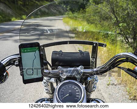 Stock Photograph - A motorcycle on the side of the road with a smart phone in a holder on the handlebars to view the map while driving; Kimberley, British Columbia, Canada. Fotosearch