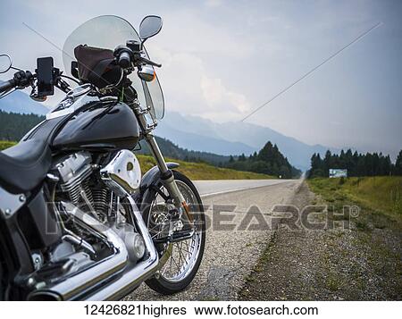 Stock Photograph - A motorcycle parked on the side of a highway with a view of the mountains in the distance; Spillmacheen, British Columbia, Canada. Fotosearch