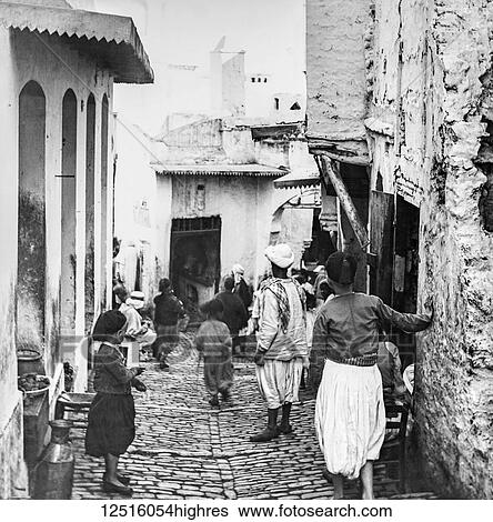 Stock Photograph - A narrow street with a cafe and pedestrians, Magic lantern slide, circa 1900; Algiers, Algeria. Fotosearch