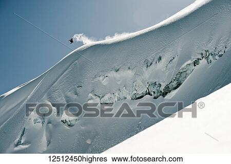 Stock Photograph - A professional, freeriding snowboarder flips mid-air on a snowy slope against a blue sky; British Columbia, Canada. Fotosearch