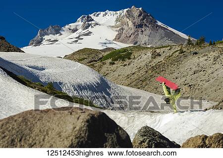 Stock Photograph - A professional, freeriding snowboarder flips mid-air on a snowy slope with rugged mountain peaks; British Columbia, Canada. Fotosearch