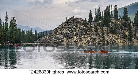 Stock Photograph - A red canoe in Moraine Lake with a cliff of the Canadian Rocky Mountains along the shoreline; Lake Louise, Alberta, Canada. Fotosearch