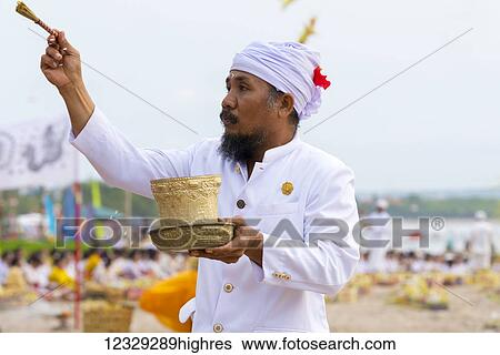 Stock Photograph - A Religious Man Sprinkles Water On Local Balinese People At A Ceremony At The Beach; Bali. Fotosearch