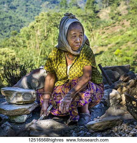 Stock Photograph - A senior woman crouches and digs in the dirt with a trowel; West Bengal, India. Fotosearch