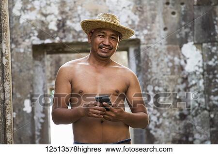 Stock Photograph - A shirtless Cambodian man holding a smart phone at Preah Vihear; Preah Vihear, Cambodia. Fotosearch