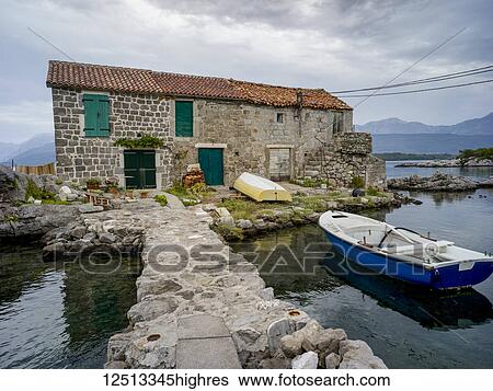 Stock Photograph - A small boat mooring outside a stone house on the Bay of Kotor; Bjelila, Opstina Tivat, Monte. Fotosearch