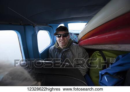 Stock Photograph - A surfer sits in the back seat of a bush plane packed with supplies and surfboards; Alaska, United States of America. Fotosearch