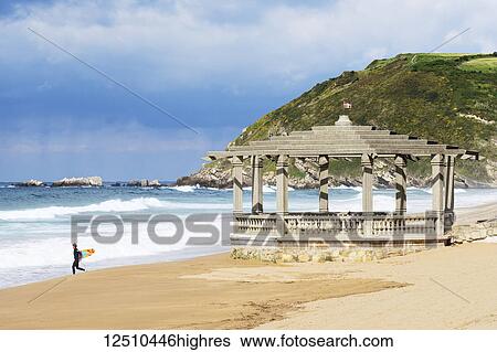 Stock Photograph - A surfer walks towards the water with a surfboard in a summer surfing area; Zarautz, Gipuzkoa, Pais Vasco, Spain. Fotosearch