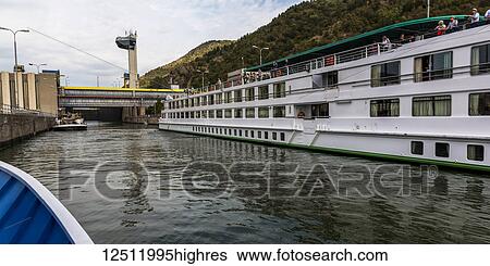 Stock Photograph - A tour boat cruises by the Iron Gate Hydroelectric Power Station, the largest dam on the Danube river and one of the largest hydro power plants in Europe; Drobeta-Turnu Severin, Jude? ul Mehedin? i, Serbia. Fotosearch
