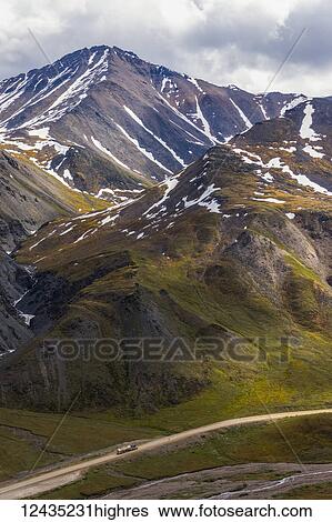 Stock Photograph - A truck approaches Atigun Pass along the Dalton Highway with the mountains of the Brooks Range towering overhead; Alaska, United States of America. Fotosearch