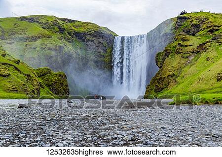 Stock Photograph - A viewpoint walking towards the iconic Skogafoss waterfall, one of the most visited places in Iceland; Iceland. Fotosearch