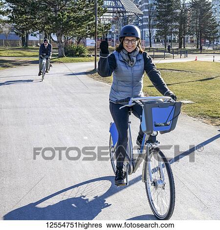 Stock Photograph - A woman cycling on a paved trail in an urban area; Vancouver, British Columbia, Canada. Fotosearch