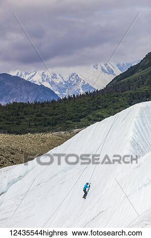 Stock Photograph - A woman ice climbs on Root Glacier in Wrangell-St. Elias National Park with Mt. Blackburn in the background; Alaska, United States of America. Fotosearch