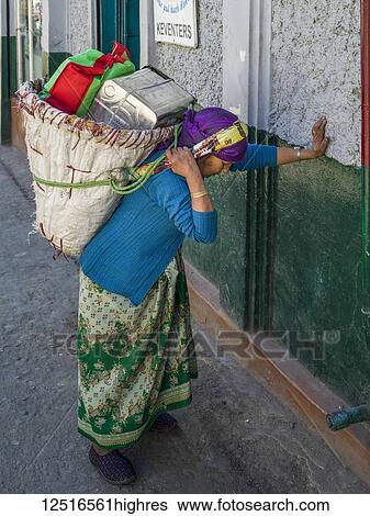 Stock Photograph - A woman pauses to rest against a wall while carrying a heavy load on her back; Darjeeling, West Bengal, India. Fotosearch