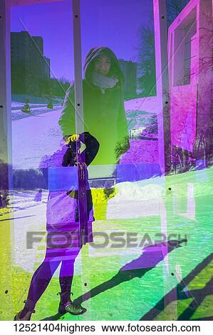 Stock Photograph - A woman takes a photo of her friend through the neon plexiglass of a Warming Hut Art Structure along the Red River Mutual Trail; Winnipeg, Manitoba, Canada. Fotosearch