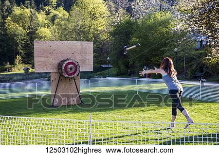 Stock Photograph - A woman throws an axe at a target at a recreational axe throwing game during a logging festival; Bowen Island, British Columbia, Canada. Fotosearch