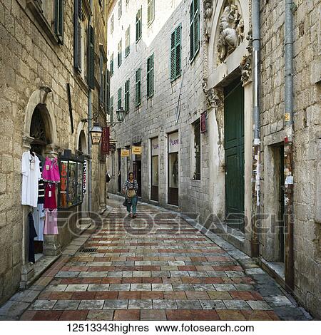 A woman walks down a narrow street between buildings with clothing on display outside a shop; Kotor, Monte View Large Photo Image Stock Photograph - A woman walks down a narrow street between buildings with clothing on display outside a shop; Kotor, Monte. Fotosearch