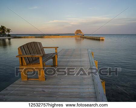 Stock Photograph - A wooden bench on a dock and open ocean at sunset; Belize. Fotosearch