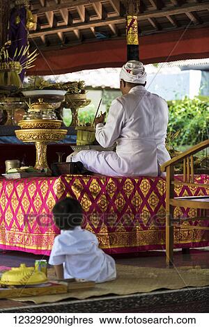 Stock Photograph - A Young Boy Sits Watching A Man Perform A Religious Ceremony; Bali, Indonesia. Fotosearch