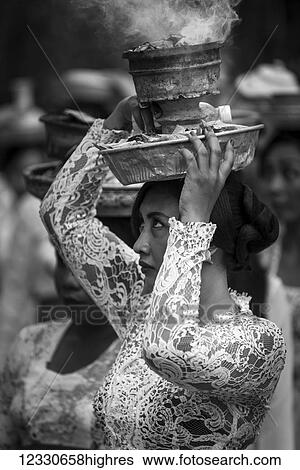 Stock Photograph - A Young Woman At A Religious Ceremony Carrying A Smoking Offering On Her Head; Bali, Indonesia. Fotosearch