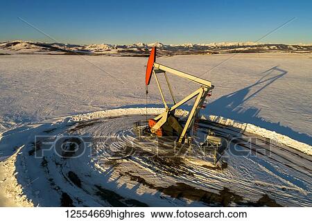 Aerial view of pumpjack in a snow-covered field with long shadows, warm light of sunrise, rolling hills, snow-covered mountains and blue sky in the background; Longview, Alberta, Canada View Large Photo Image Stock Photograph - Aerial view of pumpjack in a snow-covered field with long shadows, warm light of sunrise, rolling hills, snow-covered mountains and blue sky in the background; Longview, Alberta, Canada. Fotosearch