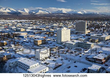 Stock Photograph - Aerial view of snow covering 3rd and 4th avenue in downtown Anchorage, the Sheraton Hotel building rising up with the Chugach Mountains in the background in winter, South-central Alaska; Anchorage, Alaska, United States of America. Fotosearch