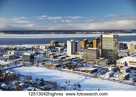 Stock Photograph - Aerial view of the snow covered park strip and buildings of downtown Anchorage in the background, sea ice surrounding Point MacKenzie in the background in winter, South-central Alaska; Anchorage, Alaska, United States of America. Fotosearch