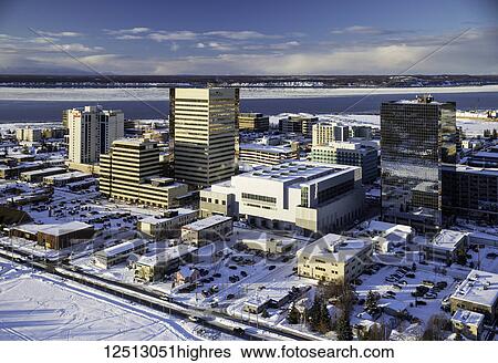Stock Photograph - Aerial view of the snow covered park strip and buildings of downtown Anchorage in the background, sea ice surrounding Point MacKenzie in the background in winter, South-central Alaska; Anchorage, Alaska, United States of America. Fotosearch