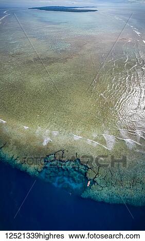 Stock Photograph - Aerial view of the southern end of the reef surrounding the island of Yap, with a dive boat anchored at Yap Caverns, a famous site for scuba divers; Ngariy, Yap, Micronesia. Fotosearch