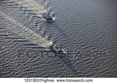 Stock Photograph - Aerial view of two tug boats sailing on the silty waters of Cook Inlet in late evening sunlight casting long shadows over the bow of the boats in winter, South-central Alaska; Anchorage, Alaska, United States of America. Fotosearch