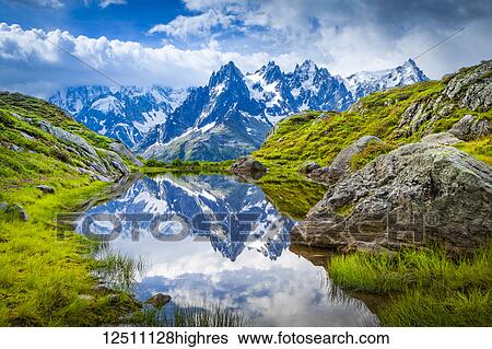Stock Photograph - Aiguille des Charmoz, part of Aiguilles de Chamonix, reflects on Lac Flegere surrounded with green meadow, Aiguilles Rouges; Chamonix-Mont-Blanc, Haute-Savoie, France. Fotosearch