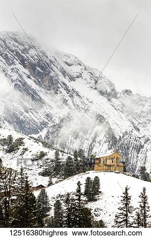 Stock Photograph - Alpine wooden castle on snow-covered ridge with a snow-covered mountain in the background; Grainau, Bavaria, Germany. Fotosearch