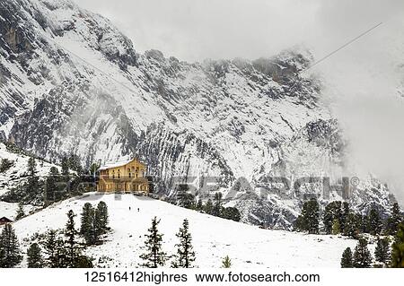 Stock Photograph - Alpine wooden castle on snow-covered ridge with a snow-covered mountain in the background; Grainau, Bavaria, Germany. Fotosearch