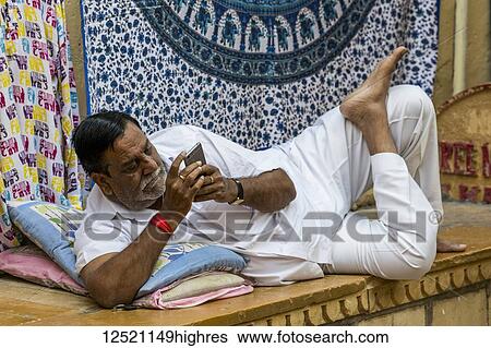 Stock Photograph - An Indian man reclines with his smart phone; Jaisalmer, Rajasthan, India. Fotosearch