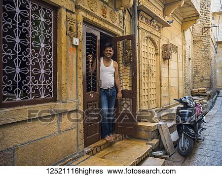 Stock Photograph - An Indian man stands in the doorway of his home with a motorcycle parked outside; Jaisalmer, Rajasthan, India. Fotosearch