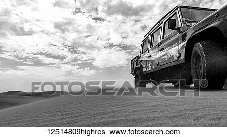Stock Photograph - Black and white image of a recreational vehicle riding over the sand dunes, Namib-Naukluft National Park; Sossusvlei, Hardap Region, Namibia. Fotosearch