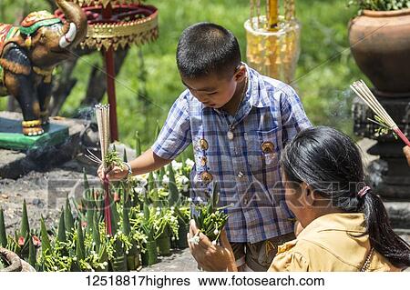 Stock Photograph - Boy with incense sticks by a Buddhist statue at the Vat Phou Temple Complex, Champasak, Laos. Fotosearch